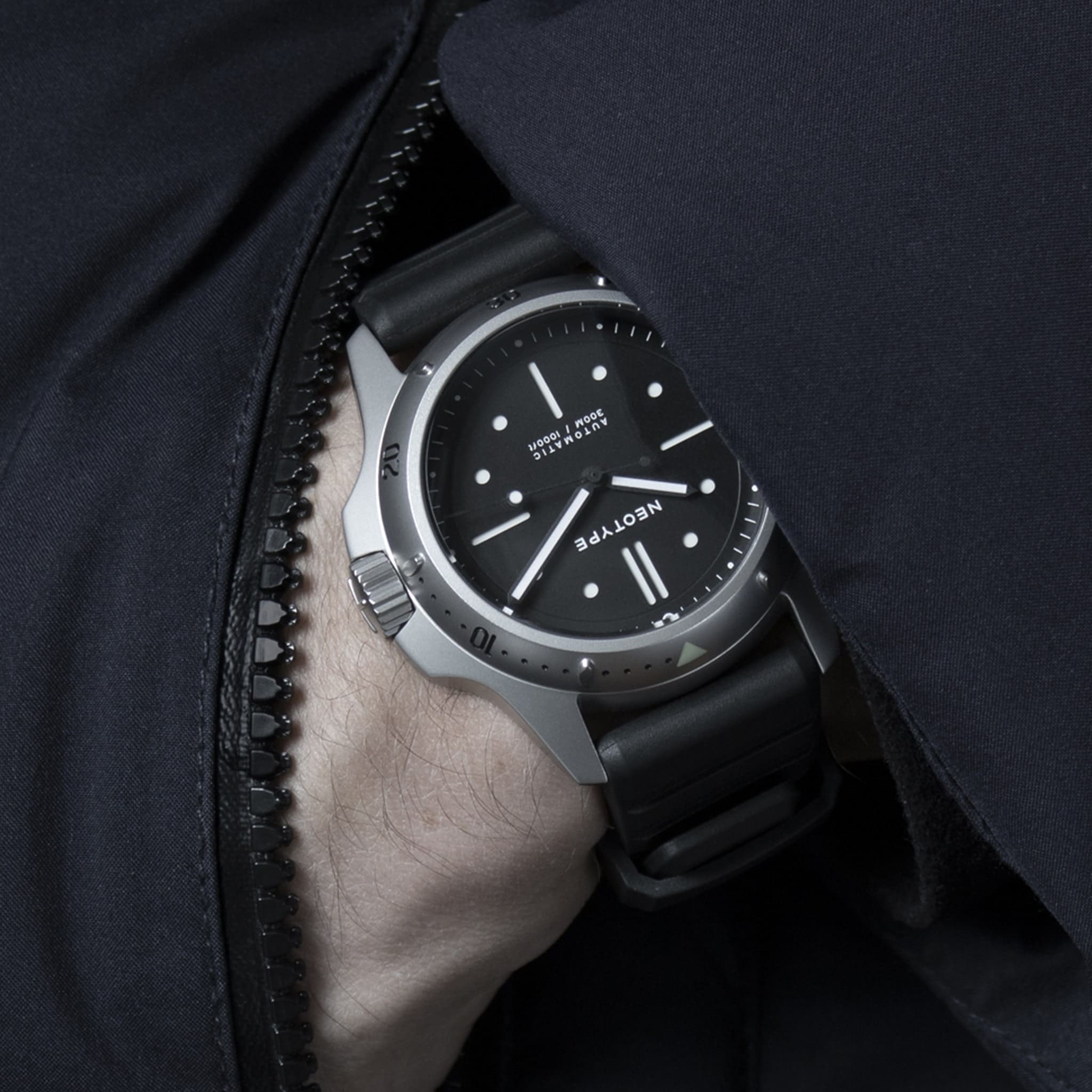 Bracelet FKM de Neotype Watches en caoutchouc fluocarboné noir, présenté en vue de face avec un emballage soigné, soulignant son design moderne et esthétique.